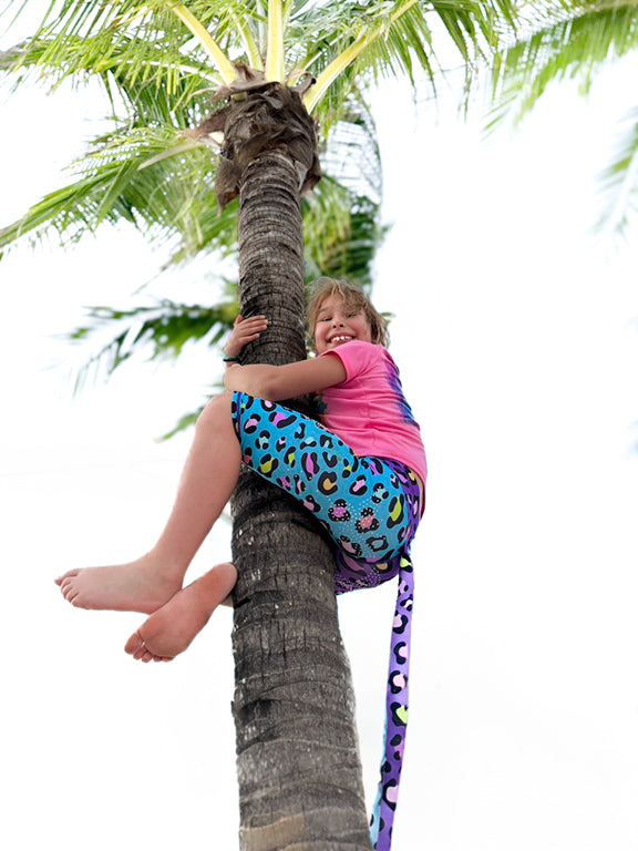Girl wearing pink and purple cheetah leggings with tail by Tailys climbing palm tree